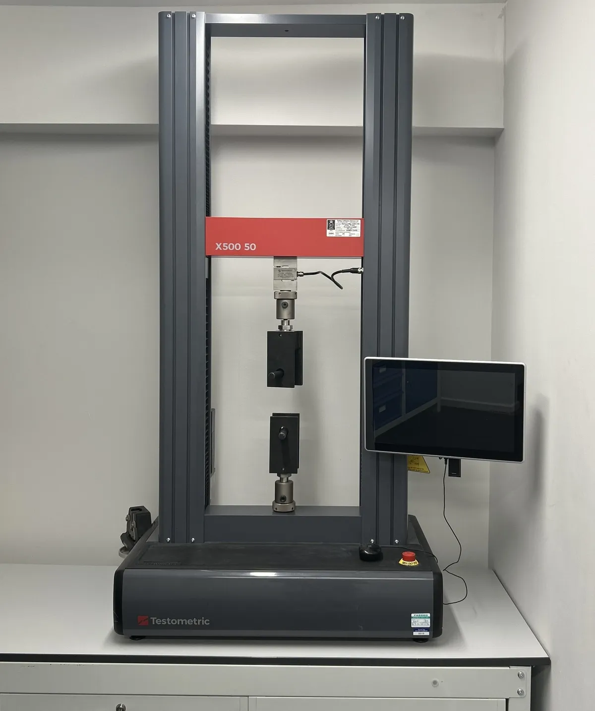The TIS tensile test machine, a tall grey frame with grips for joint test strips and a touchscreen