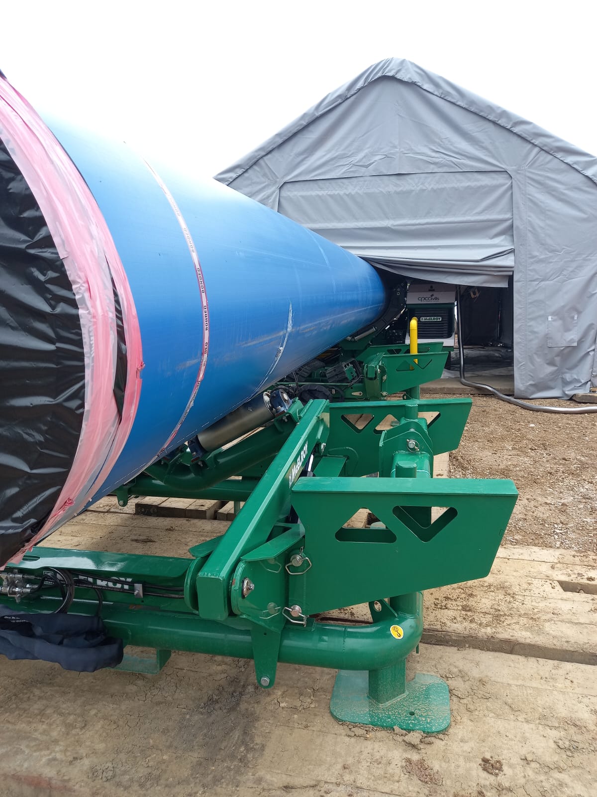 Large-diameter blue PE pipe on a green pipe handling machine beside a site tent